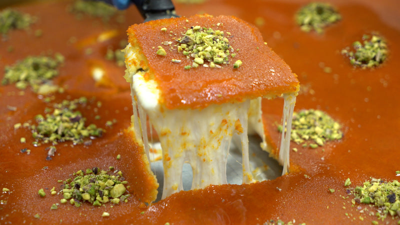 Pulling Knafeh Kunafeh from a tray exposing a cheese pull